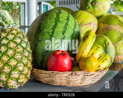 Frische Sommer Obst, Ananas, Wassermelone, roten Apfel, Orangen, Bananen und Kokosnüsse im Korb auf den Tisch. Stockfoto