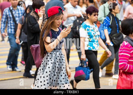 Asiatische Mädchen konzentriert sich auf mobiles Gerät, während die Kreuzung in Hong Kong, SAR, China Stockfoto