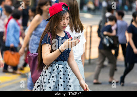 Asiatische Mädchen konzentriert sich auf mobiles Gerät, während die Kreuzung in Hong Kong, SAR, China Stockfoto