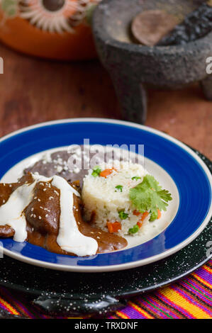 Mexicanischen Mole Sauce mit Huhn, Reis und schwarze refried Beans. Neben Zutaten wie Schokolade und Paprikas serviert. Traditionelle Speisen aus Oaxaca ein Stockfoto