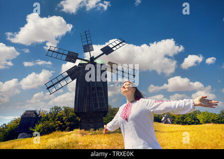 Schöne Ukrainische Mädchen in weißen ethnischen Shirt besticken Tanzen in der Nähe von Alte hölzerne Windmühle in Nationale Architektur Museum in Pirogowo, Kiew, Ukraine Stockfoto