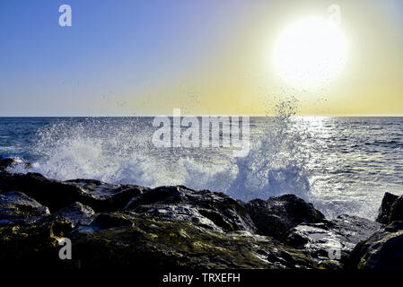 Morgendämmerung am Ufer des Meeres Wellen gegen die Felsen Spritzwasser gegen die Sonne Stockfoto