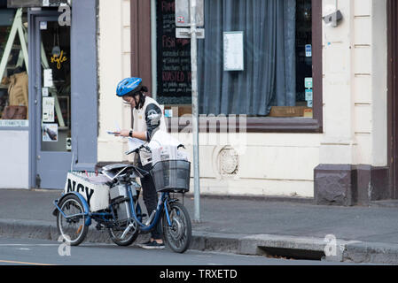 Am frühen Morgen in Fitzroy, Melbourne, Australien, eine Frau steht in der Nähe von mit Batterie Dreirad und prüft die Unterlagen während einer Zeitung Lieferung ausführen Stockfoto