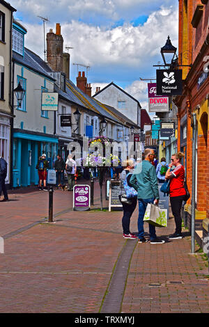 Käufer genießen Sie die Mischung aus kleinen Geschäften und traditionellen Pubs im malerischen alten Fore Street, eine der Haupteinkaufsstraßen der Stadt am Meer von Sidmouth Stockfoto