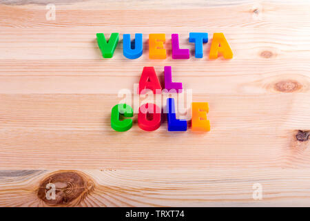 Zurück in Spanisch zur Schule, "Vuelta al Cole'. Text mit magnetischen farbigen Buchstaben über eine hölzerne Schule Tabelle geschrieben Stockfoto