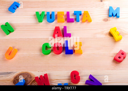 Zurück in Spanisch zur Schule, "Vuelta al Cole'. Text mit magnetischen farbigen Buchstaben über eine hölzerne Schule Tabelle geschrieben Stockfoto