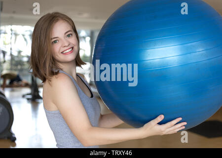 Lächelnden jungen kaukasischen Frau Mädchen mit einem blauen Gymnastikball im Fitnessstudio, Training oder Yoga Pilates Übung Stockfoto