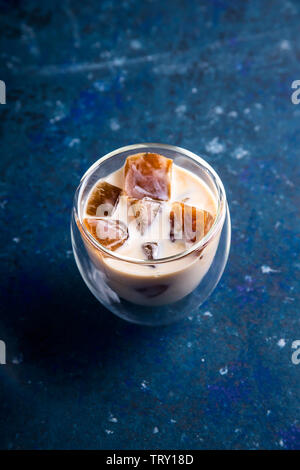 Eis Kaffee mit Milch in ein modernes Glas mit einem doppelten Boden auf einem blauen Hintergrund Stockfoto