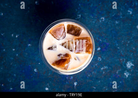 Eis Kaffee mit Milch in ein modernes Glas mit einem doppelten Boden auf blauem Hintergrund. Ansicht von oben, flach Stockfoto