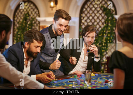 Ein junger Mann ist glücklich, im Casino zu gewinnen. Eine Gruppe von Menschen spielen Poker Roulette in einem Casino. Stockfoto