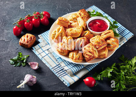 Blätterteig Brötchen mit gehacktem Hühnerfleisch und Pilze mit Ketchup und Petersilie auf einem weißen Teller auf einen konkreten Tisch serviert, Ansicht von oben Stockfoto