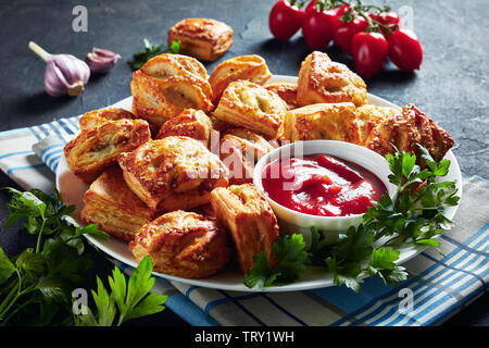 Blätterteig Brötchen mit gehacktem Hühnerfleisch und Pilze mit Ketchup und Petersilie auf einer weißen Platte auf eine Küche konkrete Tisch serviert, Ansicht von oben, Stockfoto