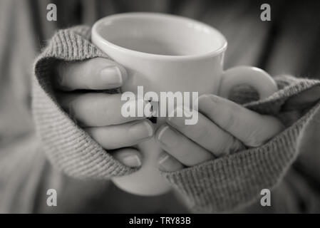 In der Nähe der Hände einer Frau in Sloppy Joe Pullover um einen Becher Kaffee verpackt Stockfoto