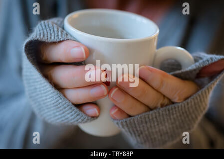 Woman's Hände in Sloppy Joe Pullover um einen Becher Kaffee verpackt Stockfoto