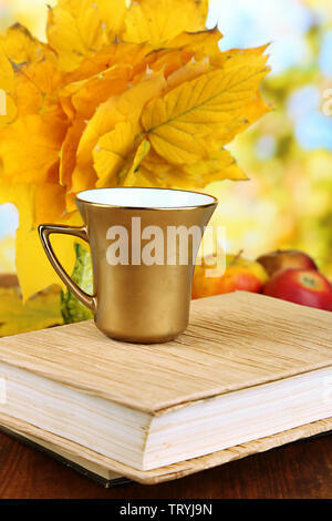 Blätter im Herbst, Tasse und Buch auf Holztisch auf natürlichen Hintergrund Stockfoto