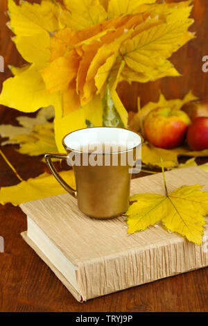 Blätter im Herbst, Tasse und Buch auf Holztisch close-up Stockfoto