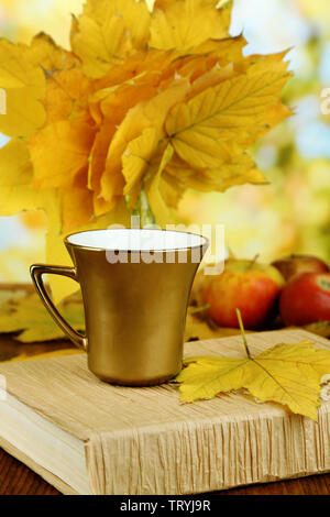 Blätter im Herbst, Tasse und Buch auf Holztisch auf natürlichen Hintergrund Stockfoto