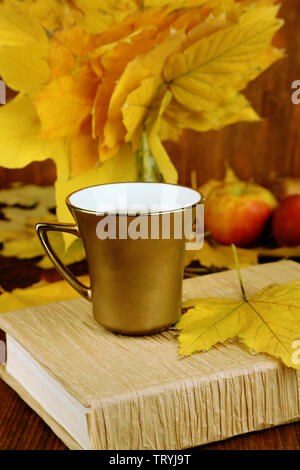 Blätter im Herbst, Tasse und Buch auf Holztisch close-up Stockfoto