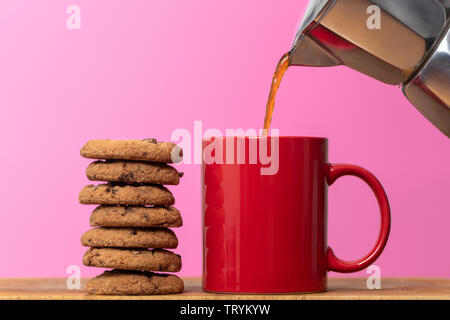 Kaffee ist ausgegossen int eine rote Tasse mit einem Stapel von Chocolate Chip Cookies Stockfoto