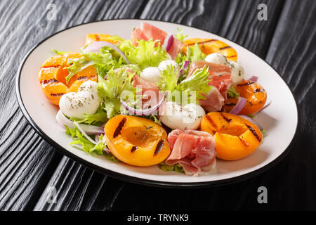 Italienischen sommers Salat mit Mozzarella, Schinken, gegrillte Aprikosen, roten Zwiebeln und Salat close-up auf einem Teller auf den Tisch. Horizontale Stockfoto