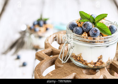 Gesundes Frühstück der Blaubeere parfaits mit frischem Obst, Joghurt, Müsli und Minze über einen rustikalen Kuchen stehen. Selektive konzentrieren. Stockfoto