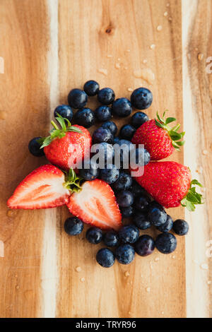 Hohe Betrachtungswinkel der Blaubeeren und Erdbeeren, in Scheiben geschnitten, auf einer hölzernen Schneidebrett. Stockfoto