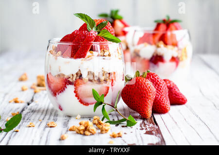Gesundes Frühstück der Erdbeere parfaits mit frischem Obst, Joghurt und Müsli über eine rustikale weißer Tisch. Selektive konzentrieren. Stockfoto
