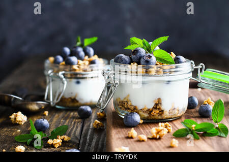 Gesundes Frühstück der Blaubeere parfaits mit frischem Obst, Joghurt, Müsli und Minze über eine rustikale Schneidbrett und Tisch. Selektive Stockfoto