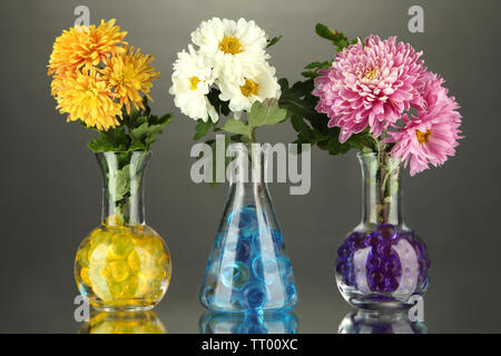 Schönen Blumen in Vasen mit hydrogel auf Tisch auf grauem Hintergrund Stockfoto