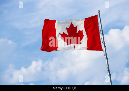 Kanadische Flagge auf der Pole in den Wind mit Wolken und blauer Himmel. Stockfoto