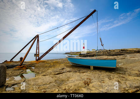 Die legendären roten Kran steht auf den Klippen in der Nähe von Portland Bill Leuchtturm mit einem türkis Boot im Vordergrund. Stockfoto