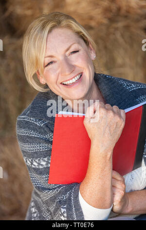 Attraktive glücklich lachend mittleren Alter Frau lachend Lächeln mit perfekten Zähne, ein Buch lesen oder Ihr Tagebuch Stockfoto