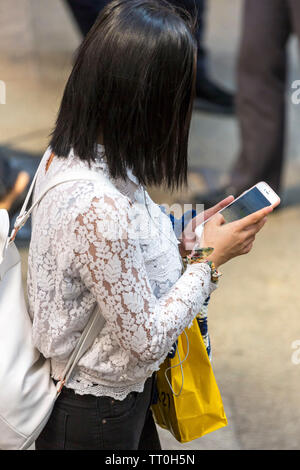 Chinesisches Mädchen konzentriert sich auf Handy Überqueren der Straße, Hong Kong, SAR, China Stockfoto