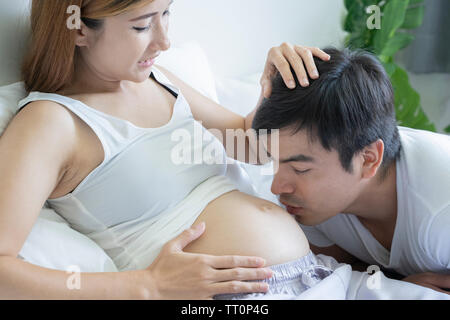 Bild der glückliche Zukunft papa Kuss den Bauch seiner fröhlichen schwangere Frau liegend auf Bett zu Hause Stockfoto