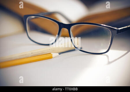 Gläser im eleganten schwarzen Rahmen, zwischen Notebooks und Bücher auf dem Tisch, beleuchtet das Sonnenlicht. Stockfoto