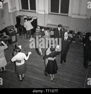 1950, historische, am Abend und einen Blick von oben auf Männer und Frauen tanzen im Ballroom Dance Class, England, Großbritannien, von einem männlichen Ausbilder beobachtet. In dieser Nachkriegszeit, vor dem Angriff der Masse Fernseher und Home Entertainment, soziale Aktivitäten wie Ballroom Dance waren beliebte Freizeit Hobbys unter einigen der erwachsenen Bevölkerung. Stockfoto