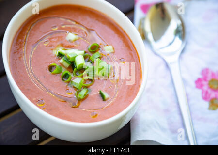 Traditionelle spanische vegan Gazpacho präsentiert auf einem Holztisch mit Olivenöl und frischen gehackten Gurken und Schalotten Stockfoto