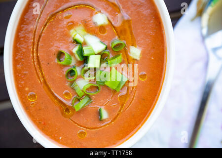 Traditionelle spanische vegan Gazpacho präsentiert auf einem Holztisch mit Olivenöl und frischen gehackten Gurken und Schalotten Stockfoto