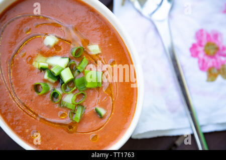 Traditionelle spanische vegan Gazpacho präsentiert auf einem Holztisch mit Olivenöl und frischen gehackten Gurken und Schalotten Stockfoto