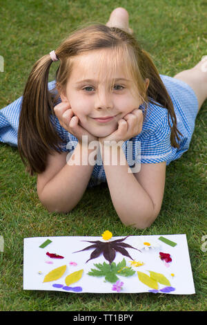 Acht Jahre alten Mädchen in Schuluniform Kleid nach der Schule, im Garten, in dem ein Bild von Blumen und Blättern auf Papier geklebt, Posing, Natur Kunst Handwerk Stockfoto