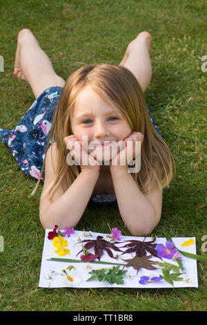 Drei Jahre alte Mädchen mit auf Gras im Garten, durch ein Bild von Blumen und Blättern auf Papier geklebt, Posing, Natur Kunst Handwerk, schauen, glücklich Stockfoto