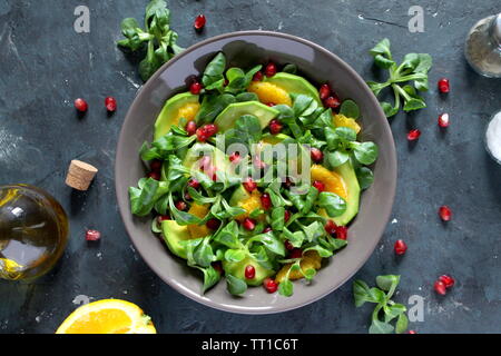 Grüner Salat mit Avocado, orange und Granatapfel in einer Schüssel auf dunklem Hintergrund. Ansicht von oben. Vegetarische und vegane Speisen. Stockfoto