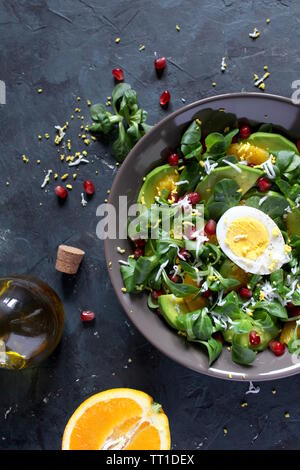 Grüner Salat mit Avocado-, Orange-, Granatapfel- und gekochte Eier in einer Schüssel auf dunklem Hintergrund. Ansicht von oben mit der Kopie. Stockfoto