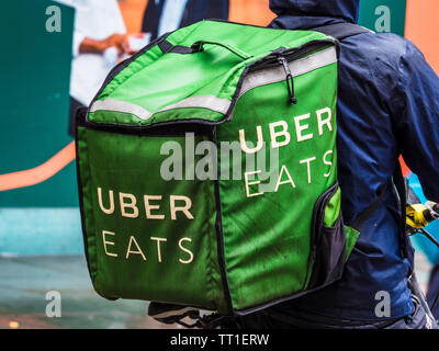 Uber isst Kurier bei schwerem Regen in London - ein Uber isst Food Delivery Kurier immer sonnigen ein heftiger Platzregen Stockfoto