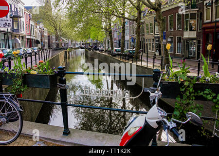 Gouda, Holland, Niederlande, April 23, 2019, Fahrräder und in der Nähe einer Brücke entlang einer Straße geparkt, Canal in Gouda Altstadt. Blumen in einem blumenbeete, Boot Stockfoto