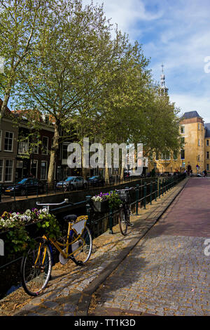 Gouda, Holland, Niederlande, April 23, 2019, Fahrräder und in der Nähe einer Brücke entlang einer Straße geparkt, Canal in Gouda Altstadt. Blumen in einem blumenbeete, Boot Stockfoto