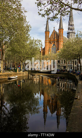 Gouda, Holland, Niederlande, April 23, 2019, Gouwekerk Kirche in der Nähe einer Brücke an einem Kanal in Gouda Altstadt. Blumen in einem parterres, Boot auf dem Wasser. Stockfoto