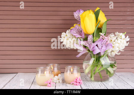 Blumen in der Vase mit Kerzen auf dem Tisch auf hölzernen Hintergrund Stockfoto