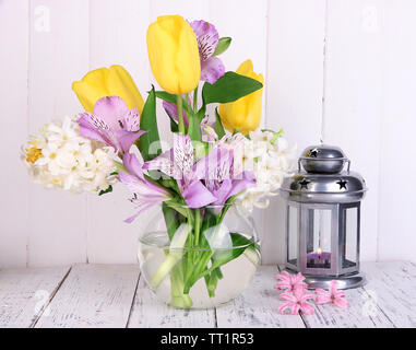 Blumen in der Vase mit dekorativen Laternen am Tisch auf hölzernen Hintergrund Stockfoto