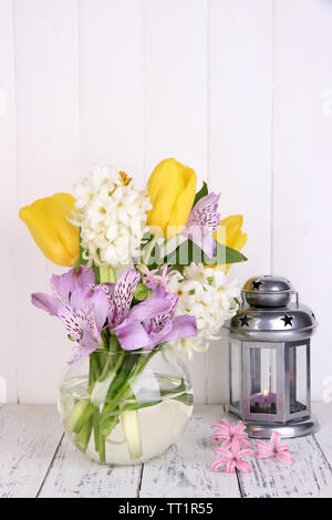 Blumen in der Vase mit dekorativen Laternen am Tisch auf hölzernen Hintergrund Stockfoto